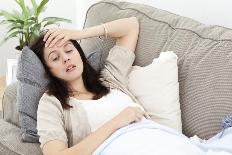 Indisposed woman feeling her temperature while resting on the so